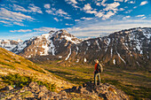 Hiker on rock outcrop overlooks Powerline Pass valley and trail, Chugach State Park, Southcentral Alaska