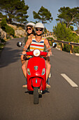 Young couple riding a red scooter on a coastal road along the Cap de Formentor peninsula, Palma, Mallorca, Balearic Islands, Spain