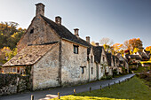 The midday sun casts its light across a row of medieval houses at Arlington Row, Bibury in Gloucestershire, Cotswolds, England, United Kingdom, Europe