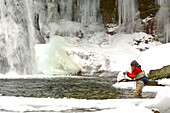 A young woman fly fishes on a cold, snowy winter day.
