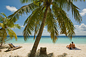 A couple relaxes on the beach at an island resort in South Male Atoll, Maldives.