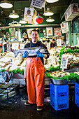 A man holds a large salmon at his stand at Pike Place Market in Seattle, WA.