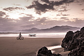 Deserted beach in a bay with cyclist and fishing boat after sunrise, Java, Indonesia