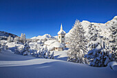 The winter sun illuminates the snowy landscape and the typical church, Maloja, Engadine, Graubunden Grisons Canton, Switzerland, Europe