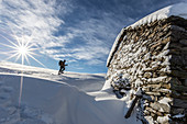 Snowshoe hiker walking near snow covered hut, Motta di Olano, Gerola Valley, Valtellina, Orobie Alps, Lombardy, Italy, Europe