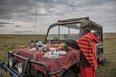 Black man having picnic on hood of car in remote field