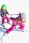 Mädchen zieht Jungen beim Skifahren auf der Piste, Pfronten, Allgäu, Bayern, Deutschland