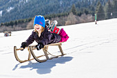 Junge liegt beim Schlittenfahren auf seinem Holzschlitten, Pfronten, Allgäu, Bayern, Deutschland