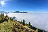 Personen sitzen am Gipfel des Großen Riesenkopf, Nebel im Tal, Mangfallgebirge mit Wendelstein im Hintergrund, Großer Riesenkopf, Mangfallgebirge, Bayerische Alpen, Oberbayern, Bayern, Deutschland
