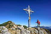 Frau geht auf Gipfelkreuz des Peitingköpfl zu, Sonntagshorn im Hintergrund, Peitingköpfl, Chiemgauer Alpen, Salzburg, Österreich