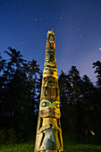 A large Totem Pole lit up at night in Sitka National Historic Park with star trails overhead, Sitka, Southeast Alaska, USA, Summer
