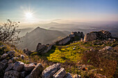 Ruins of a stone wall and buildings with a sunburst and mountains, Corinth, Greece