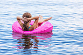 Girl resting in pink inflatable ring on Balsam Lake, Ontario, Canada