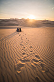 Couple watching the sunset over sand dunes in the desert at Huacachina, Ica Region, Peru, South America