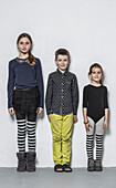 Full length portrait of smiling brother with sisters standing side by side against wall