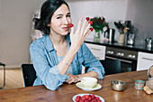 Portrait of happy young woman holding raspberries on fingers at home