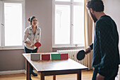 Young woman playing table tennis with man at home