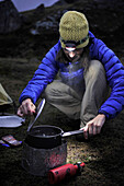 Woman hiker prepares a meal at camp during a backpacking trip to Reed Lakes in the Talkeetna Mountains near Palmer, Alaska August 2011.