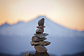 The blurred outline of Mount Baker frames a summit cairn built of rock.