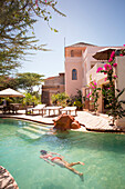 A young woman swims underwater in a small resort's light green pool.