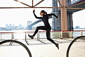 Caucasian runner jumping on waterfront, New York, New York, United States