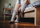 Caucasian woman sitting on bed pulling up socks