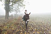 Girl riding donkey on field during foggy weather