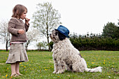 Full length side view of girl eating in front of dog on field