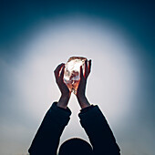 Cropped hands of man holding ice against sky at dusk