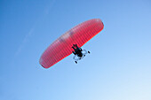 Low angle view of person motor paragliding against clear blue sky