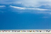 Hooded beach chairs on shore against cloudy sky