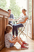Girl sitting on floor with digital tablet as parents chat in background