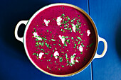 Directly below shot of beetroot soup served in cooking pan on blue table