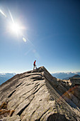 A hiker walks along a rocky ridge while on the summit of Cassiope Peak near Pemberton, British Columbia, Canada.