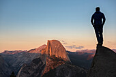 Man standing on a rock looking at Half Dome in sunset light. Yosemite, CA, USA.