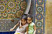 zwei lächelnde Mädchen vor einer Wand mit bunten Kacheln, Souk, Fes, Marokko