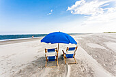 2 Liegestühle und ein Sonnenschirm in blau bieten einen einsamen Platz am weitläufigen Strand von Isle of Palms, Charleston, South Carolina, USA