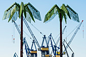 Two metal palm trees in the green area Park Fiction on the border Altona Old Town to St. Pauli with look at cranes of the shipyard Blohm and Voss, Hamburg, Germany