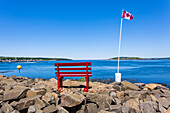 Ein ruhiger Platz mit roter Bank und kanadischer Nationalflagge am Nordatlantischen Ozean, Digby, Nova Scotia, Kanada