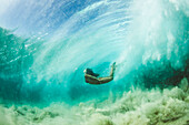 Full color photo of a girl in a bikini swimming underwater in the ocean.  She goes underneath the waves over a sandy bottom covered by clear water.