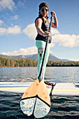A young woman paddle boards on a pond in Maine.
