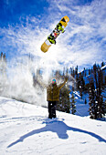 A man throws his snowboard in the air and spreads his arms on a sunny day in the Wyoming backcountry.