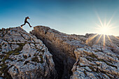 Hiker jumping over a crevice, near Falzarego Mountain Pass, Dolomites, Unesco world heritage, Italy