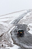 A car negotiates a road through a wintry landscape in the Elan Valley area in Powys, Wales, United Kingdom, Europe