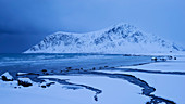 Verschneite Landschaft am Strand von Flakstad mit dem Gipfel des Hustinden (691 m) im Winter, Flakstadøya, Lofoten, Norwegen, Skandinavien