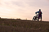 Junge Frau schiebt ihr Fahrrad über ein Feld