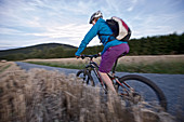 Junge Frau fährt Fahrrad auf einem Weg zwischen Feldern