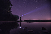 Young man standing at a lake and looking towards the stars, Freilassing, Bavaria, Germany