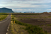 Two tourists walk the desert Hringvegur road by motorbike. They are direct to cliffs of Dyhrolaey, on background. iceland