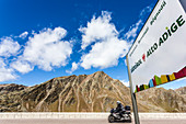 A motorcyclist passes the border sign on the pass Timmelsjoch Highalpinestreet, Hochgurgl, Ötztal, Tyrol, Austria, South Tirol, Alto Adige, Italy